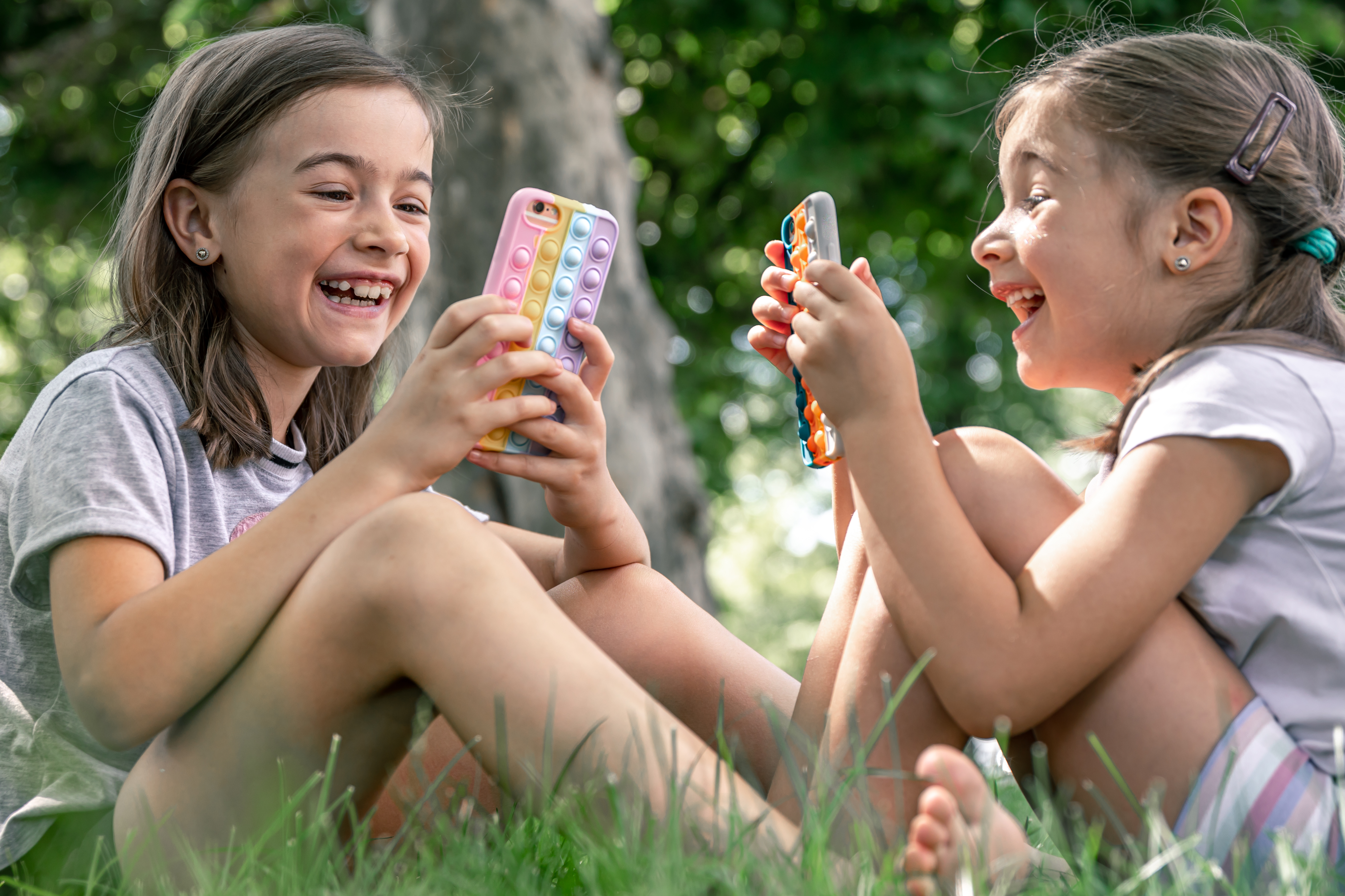 Little girls outdoors with phones in a case with pimples pop it, a trendy anti stress toy.